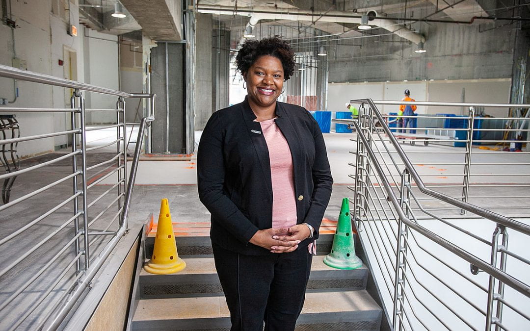 African American woman smiles and stands in a concrete building interior under construction