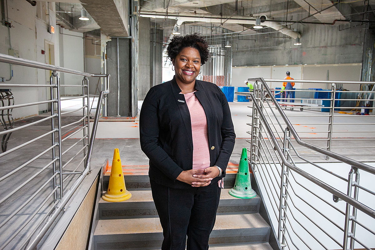 African American woman smiles and stands in a concrete building interior under construction 