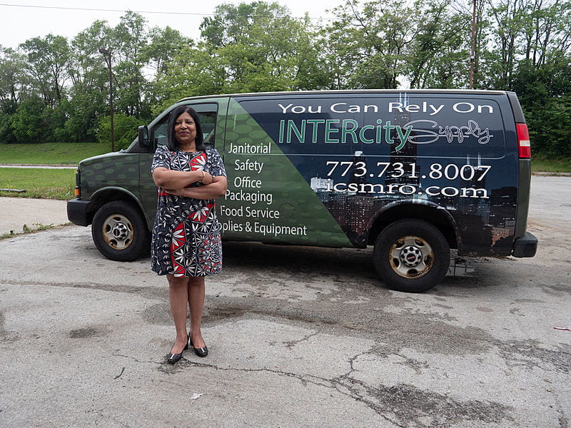 African American woman in dress stands in front of a van reading "You Can Rely on Intercity Supply"